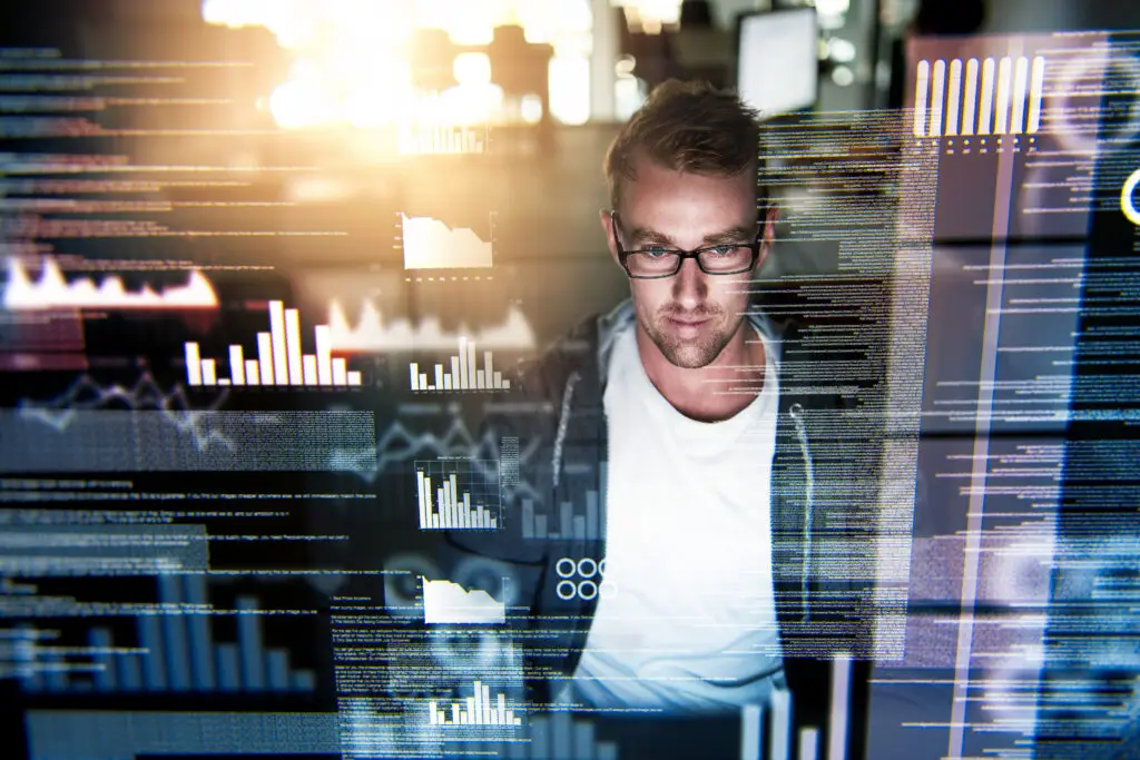 Mann arbeitet konzentriert am Computer mit eingeblendeten Daten, Codezeilen und Diagrammen